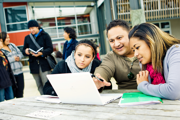 An educator instructing his learners with the aid of a laptop outside the campus.